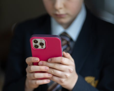 A young person in school uniform holds a red-cased iPhone with both hands