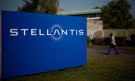 A man walks past a blue and white sign for Stellantis