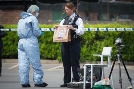 Police and forensic officers holding an evidence bag, at the scene at a car park in Hampton.