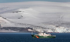 A Greenpeace ship afloat on the Ocean with snow-covered land rising up behind