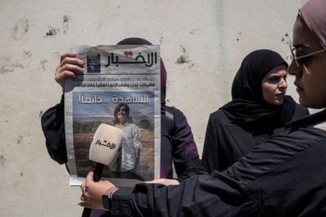 एक महिला अखबार के सामने माइक्रोफोन रखती है जिसमें पहले पन्ने पर अमल खलील की तस्वीर है।