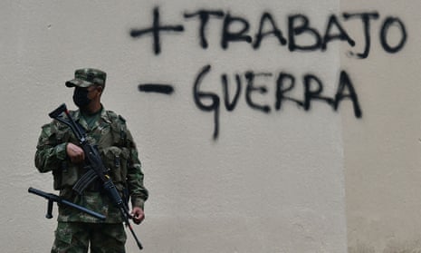A soldier stands guard in front of graffiti saying plus trabajo,  minus guerra