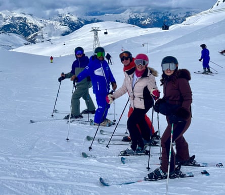 Five skiers pause on a snowy slope with mountains behind