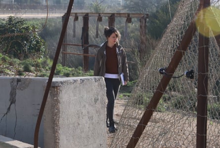 Bethan McKernan walks along a dirt track surrounded by chainlink fence, concrete blocks, barbed wire