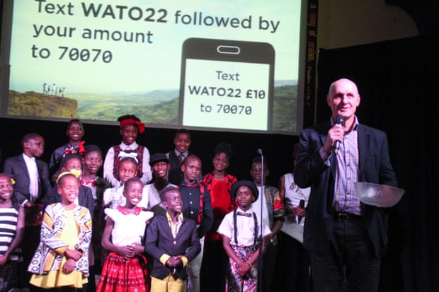 Pastor Bruce Stoke of Woodgrange Baptist Church, London, addresses the audience after a Watoto Choir performance, in front of a screen calling for donations