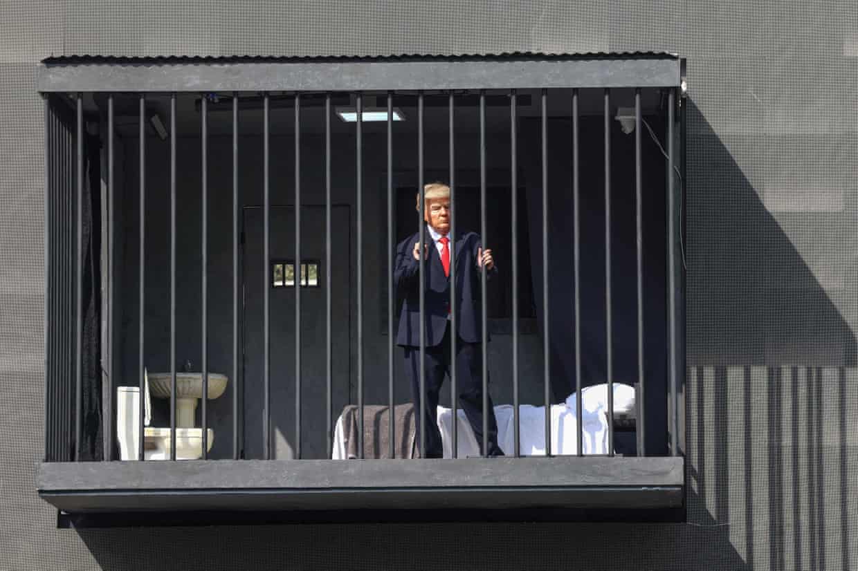 An Iranian actor in a Trump mask stands behind bars in a mock prison cell billboard
