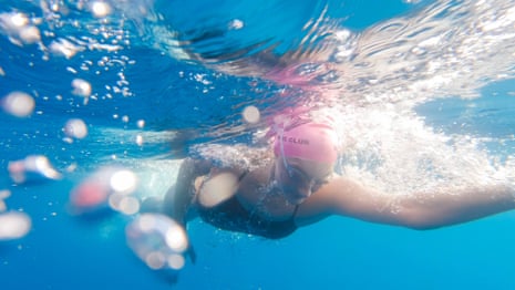 Open water swimmer Catherine Breed swims underwater, surrounded by bubbles and sunlight.