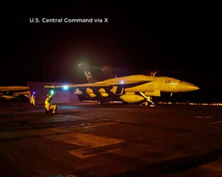 A military fighter jet prepares for launch from an aircraft carrier runway at night