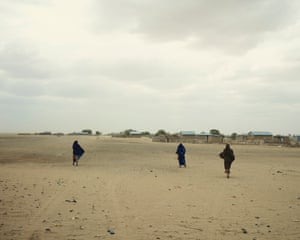 Women walk an open landscape of sand to Korbesa village