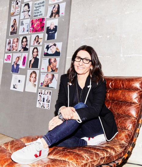 Bobbi Brown sitting on a reclining chair, smiling, wearing jeans and white trainers, a board of photos to her side