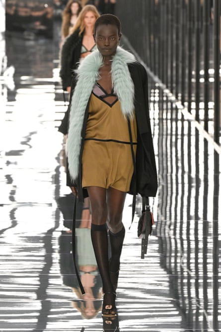 A model wearing a silky gold/brown mini dress with a neckline that leaves the bra underneath on show, with a blue fluffy fur stole around her shoulders, on the catwalk at Milan fashion week.