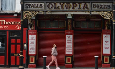 A woman in pink leggings and a face mask walks past the theatre's red roller doors  in March this year.