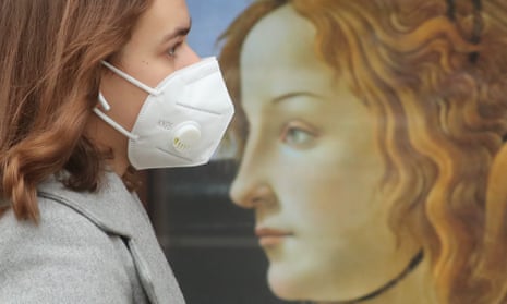 A woman wearing a face mask walks past a mural during the ongoing COVID-19 pandemic