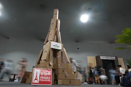 Attenders walk past boxes made to look like the Eiffel Tower with a sign that reads “1.5 degrees Celsius under threat” at Cop30