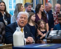 a man speaks while seated at a desk with a jug of milk on it