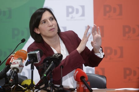 Elly Schlein during a press conference with a large Italian flag behind her