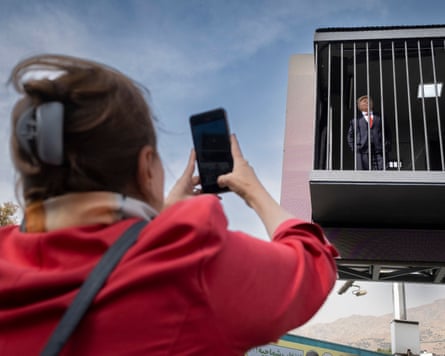 An Iranian woman films a man performing as Donald Trump inside a symbolic cell mounted on a billboard in northern Tehran