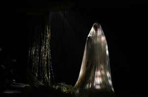 A model wearing a white dress and completely covered by a veil walks the runway