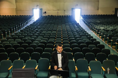 Man in tux sitting in empty auditorium on a laptop.