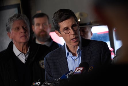 man speaks into reporters’ microphones as others look on