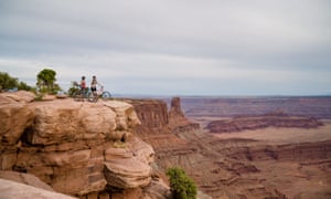 Wide shot image of two cyclists admiring the view at the edge of a cliff overlooking a canyon