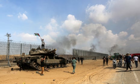 Palestinians wave their national flag and celebrate by a destroyed Israeli tank at the Gaza Strip fence east of Khan Younis in southern Israel on Saturday