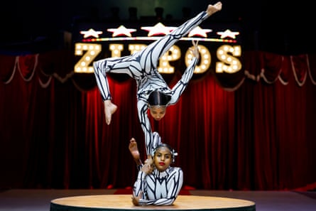 Two contortionists perform, with one balancing on top of the other on one hand looking disinterested