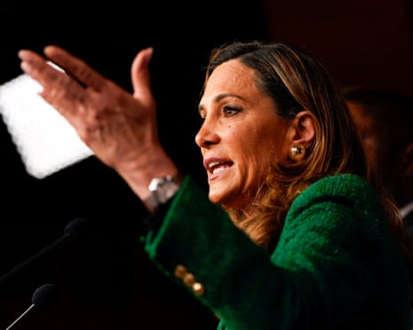 woman in green jacket speaks into microphone with hand gestured
