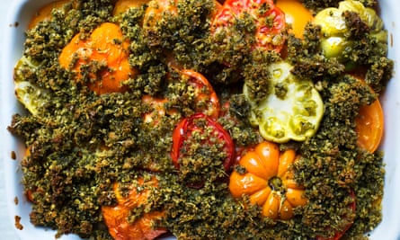 Large orange, red and green tomato slices protruding through a dark green basil crumb mixture
