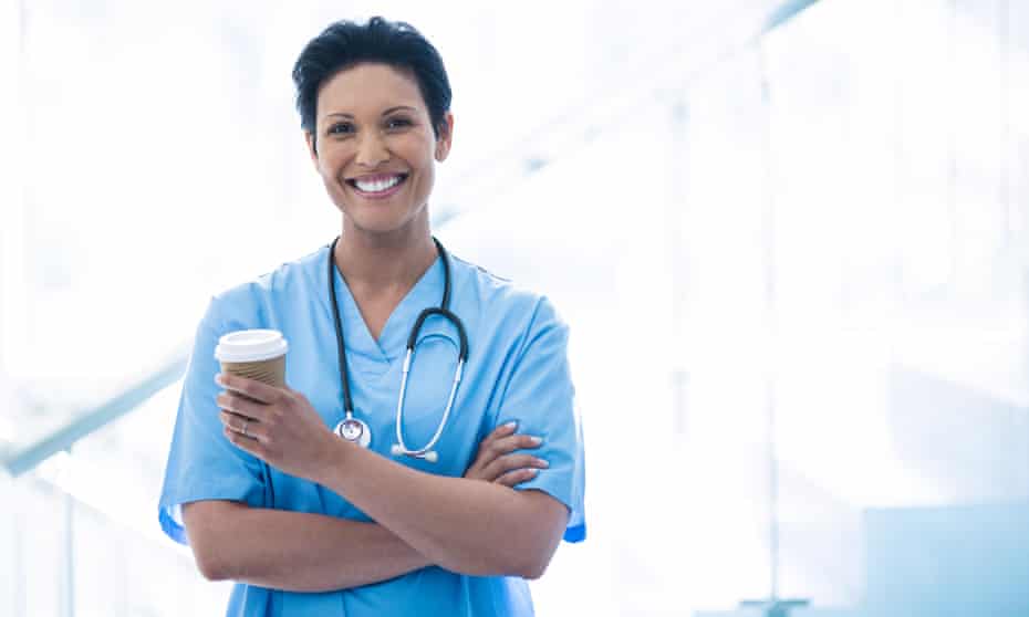 Female nurse standing with disposable cup in corridor
