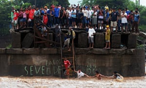 People try to cross a river as others look from a damaged bridge in El Salvador in the wake of Tropical Storm Agatha, which led to consumption per head falling by 5.5% and increased poverty by 14%. 