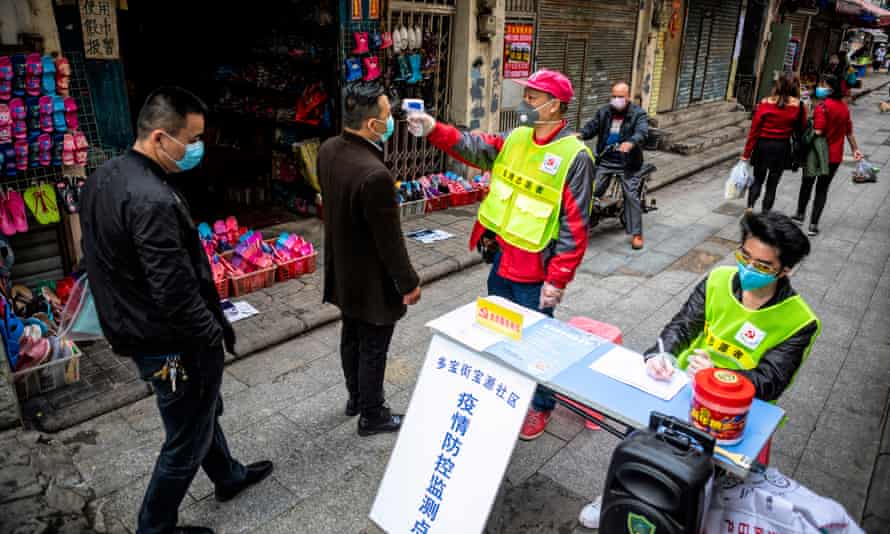 A man measures people’s body temperature at a roadblock in Guangzhou, China