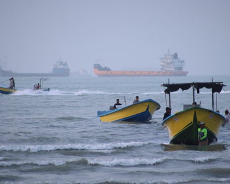 Ships lie anchored in the strait of Hormuz, with smaller boats in the foreground.