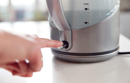 A woman presses the power switch on an electric kettle