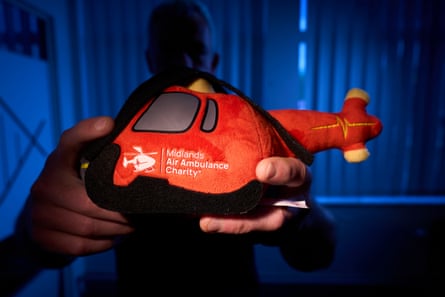 A man in shadows holds out a bright red soft toy in the shape of a helicopter, with the Midlands air ambulance logo on the side.