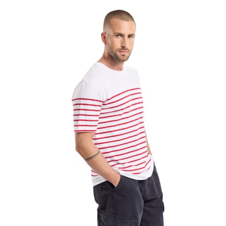 A model wears a men’s Amor-lux “Etel” Breton striped shirt. The T-shirt is short sleeved =, white with red horizontal stripes from the armpit line to the base.