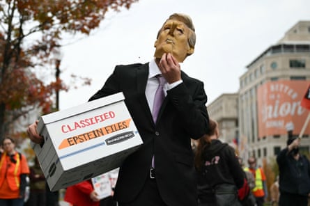 A protester wearing a Trump mask with a Pinocchio nose and carrying a box reading ‘Classified Epstein Files’
