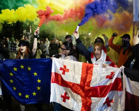 People waving flags surrounded by coloured smoke