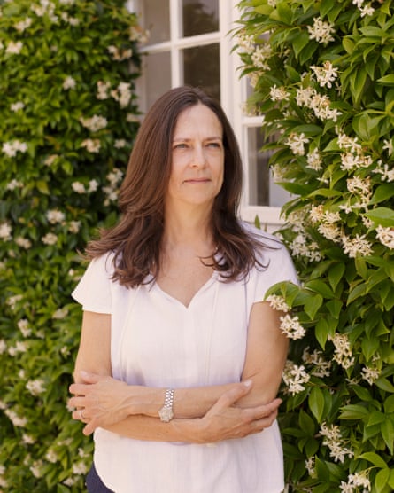 Portrait of Sarah Kitt  wearing a summer top and standing in front of a flowering plant