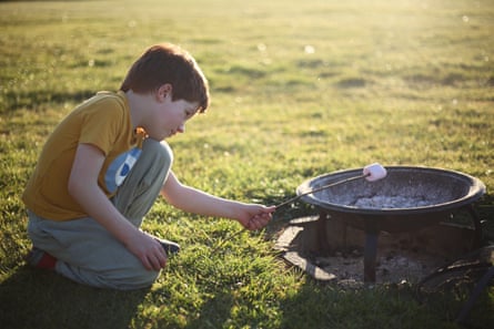 A child puts a marshmallow on a stick over a campfire