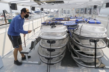 A man pulls on a rope securing transparent kayaks on a boat.