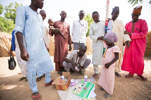 People stand watching as a local worker gets out a trachoma treatment kit, Nigeria