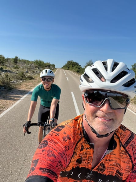 Two men in helmets cycling on a road.