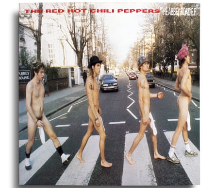 The four band members of the Red Hot Chili Peppers walk in single file across a zebra street crossing. They are completely naked except for strategically placed white tube socks covering their penises