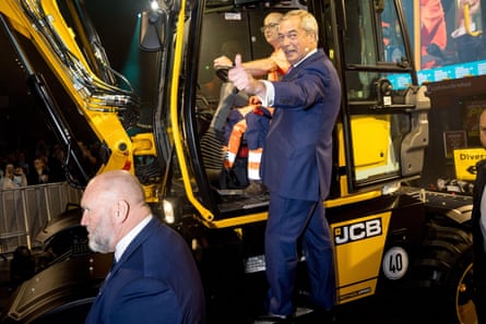 Farage in a blue suit stands on the side of a JCB digger and greets a crowd