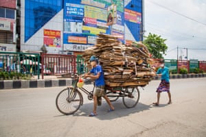 A masked man pushes an overladen rickshaw along a wide but quiet street in Dhaka