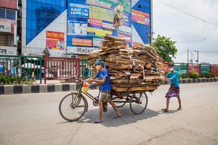 A masked man pushes an overladen rickshaw along a wide but quiet street in Dhaka