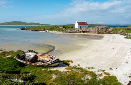 A sandy cove with a small beached boat in the foreground and a small white house with red roof in the distance