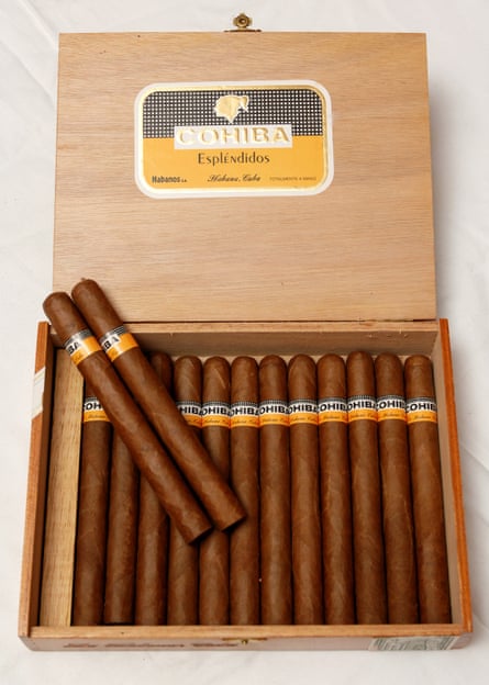 Wooden box containing Cohiba Cuban cigars, which have a yellow, black and white label on them and the logo on the lid of the open box.