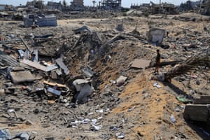 A person stands and looks into a big crater full of the debris of buildings